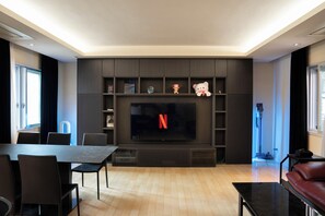 A modern living room with a flat-screen TV, dark wood shelving, a dining table with chairs, and a leather sofa. - SHIBUYA CITY HOUSE (Tokyo)