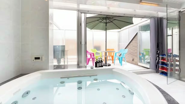 Ein moderner Poolbereich im Innenbereich mit Whirlpool, bunten Liegestühlen und einer Glastür zu einem Außenbereich.
