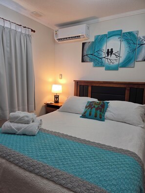 Ein Hotelzimmer mit einem Bett, einem Nachttisch, einer Klimaanlage und Kunstwerken an der Wand.