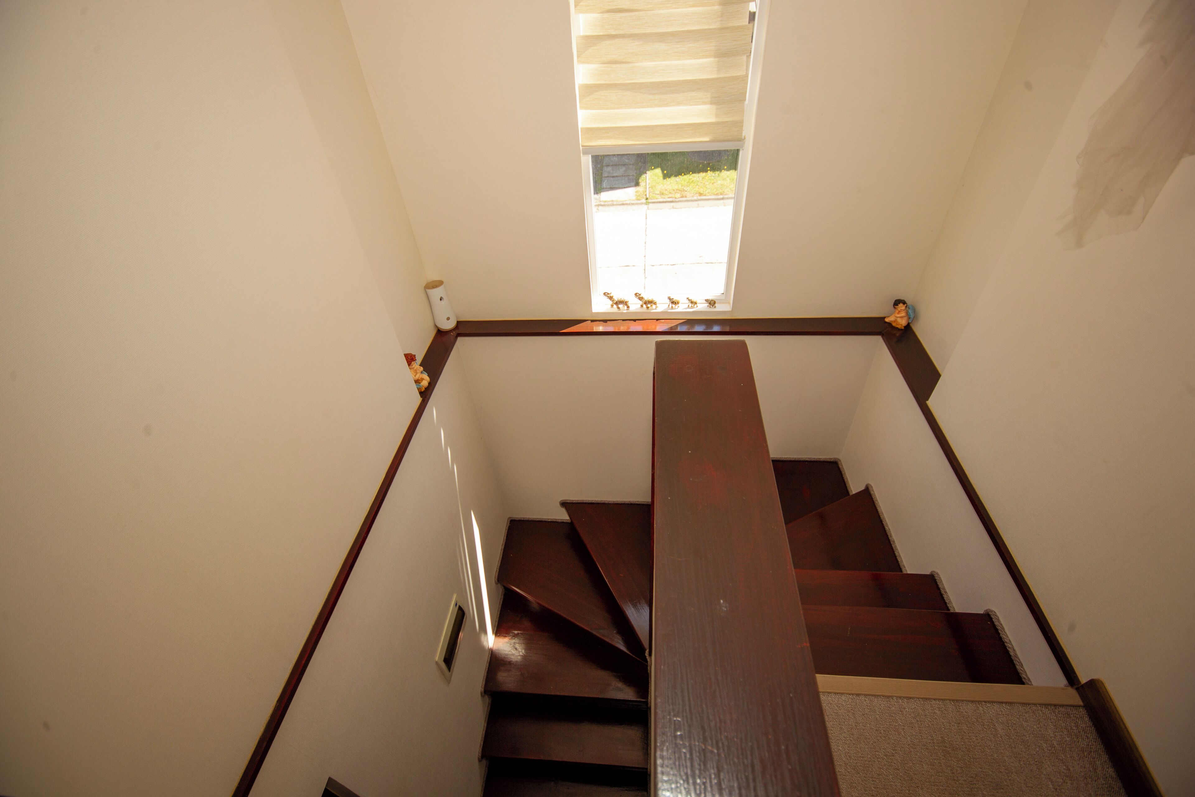 A wooden staircase with a handrail, a small window with blinds, and a wall-mounted light fixture.