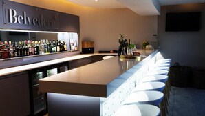 Una zona de bar con una barra alargada, varios taburetes y una amplia selección de botellas.