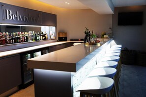 A bar area with a long counter, multiple stools, and a variety of bottles. - Northstar Hotel (uMhlanga)