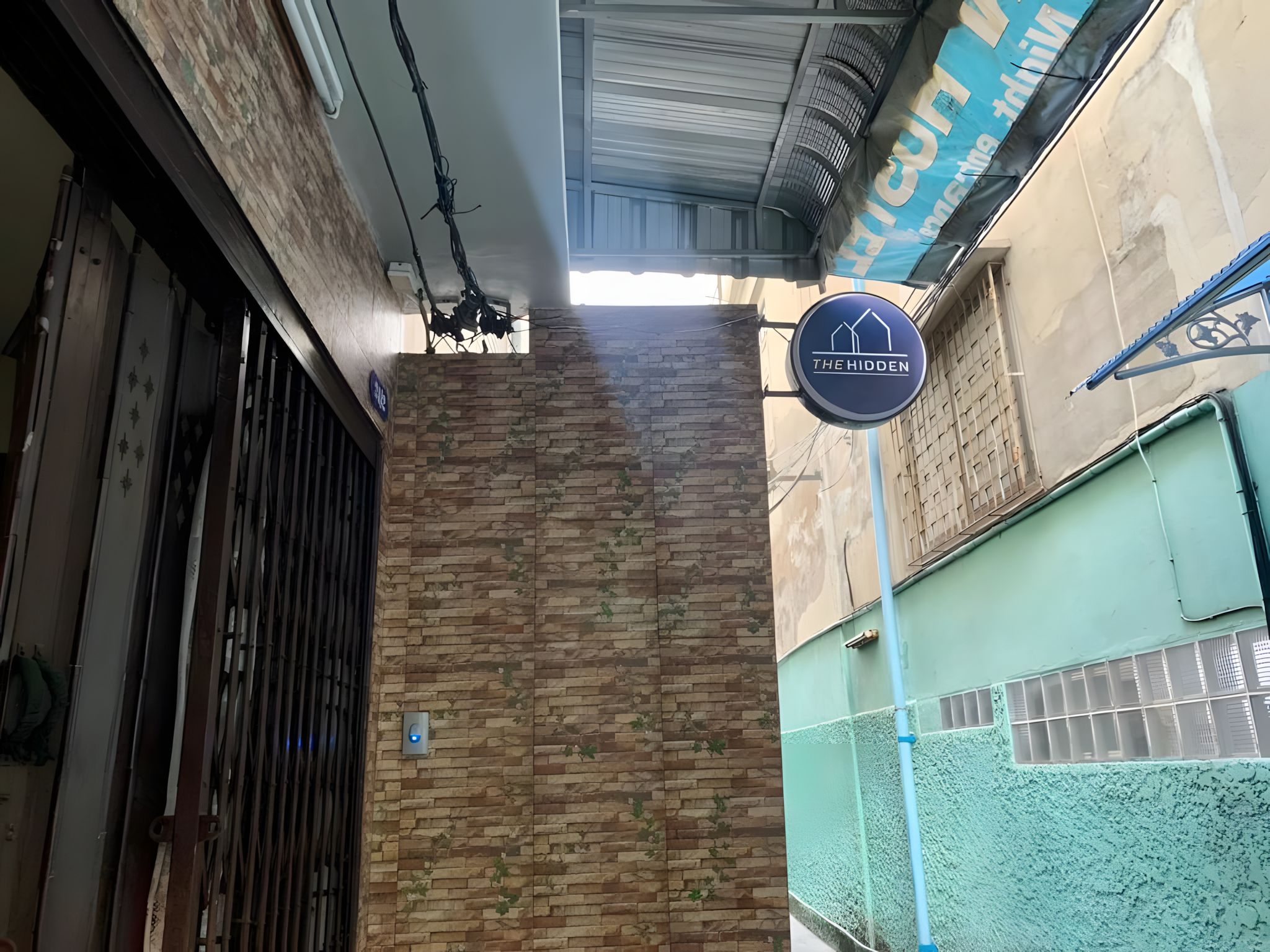 A building facade with a brick wall, a metal gate, and a sign for 'The Hidden'.