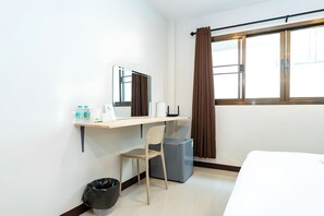 Ein Hotelzimmer mit Schreibtisch, Stuhl, Mülleimer und einem Bett.