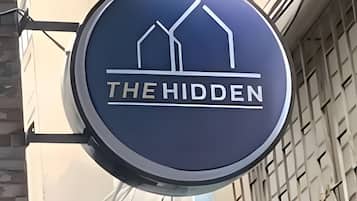 A circular sign with the text 'THE HIDDEN' and a graphic of two buildings.