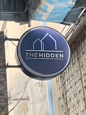 A circular sign with the text 'THE HIDDEN' and a graphic of two buildings. - The Hidden Giant Swing (Bangkok)