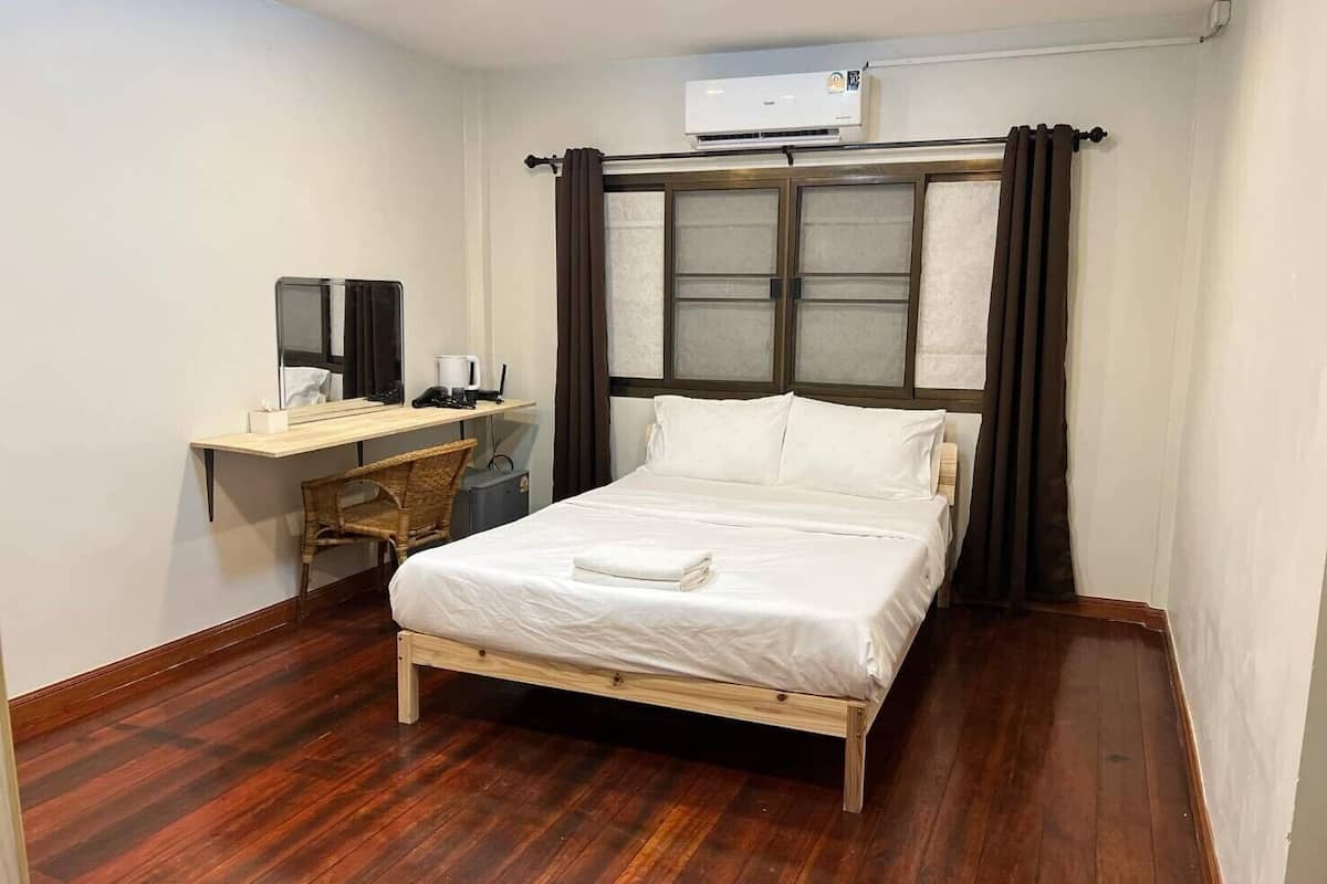 Een hotelkamer met een houten bed, een bureau met stoel, een klein tafeltje en een airconditioning.
