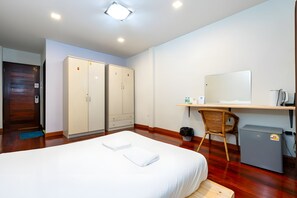 A hotel room with a bed, a desk with a computer, a chair, a small fridge, and a wardrobe. - The Hidden Giant Swing (Bangkok)