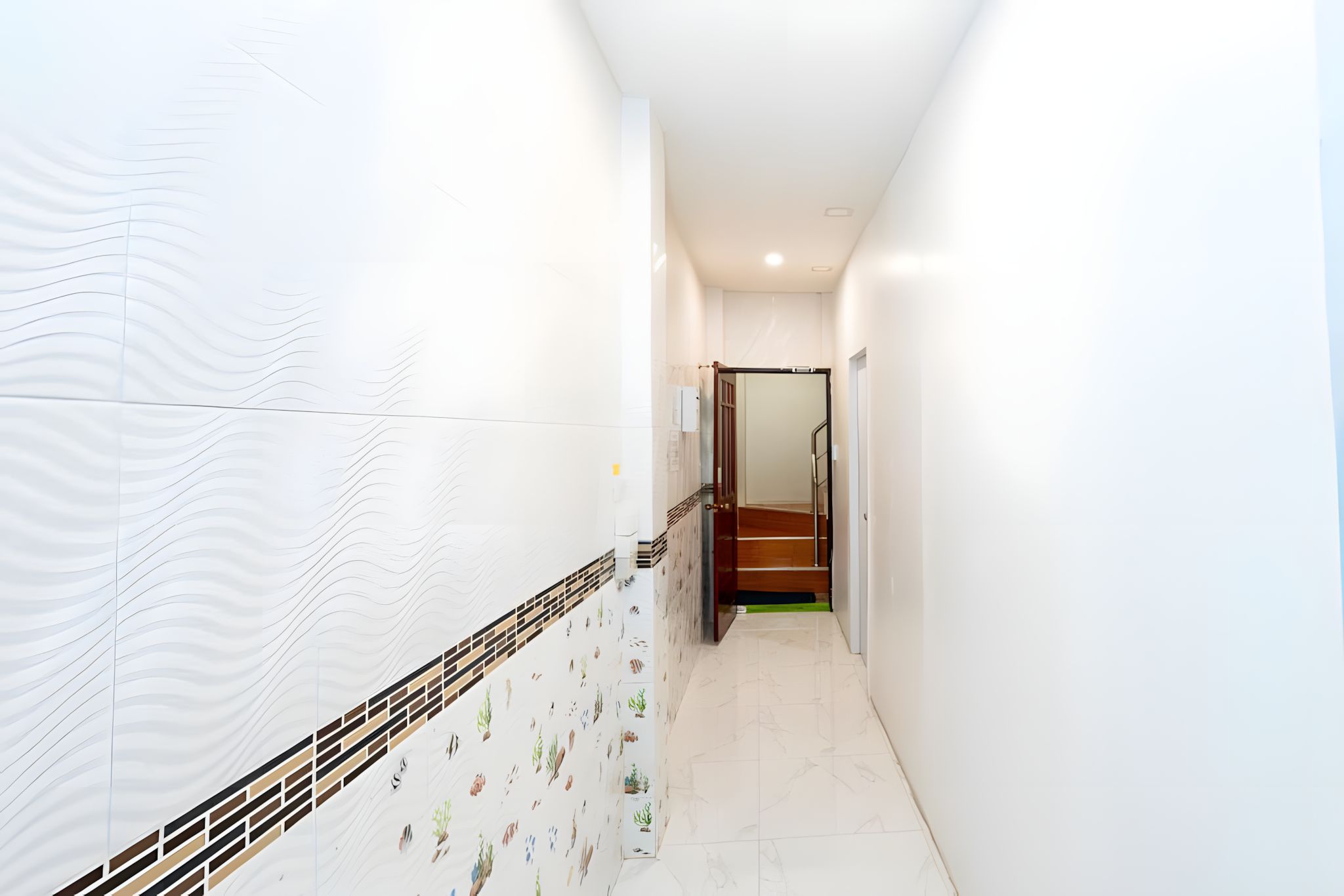 A narrow hallway with white walls and a tiled floor, leading to a staircase.