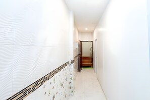 A narrow hallway with white walls and a tiled floor, leading to a staircase. - The Hidden Giant Swing (Bangkok)