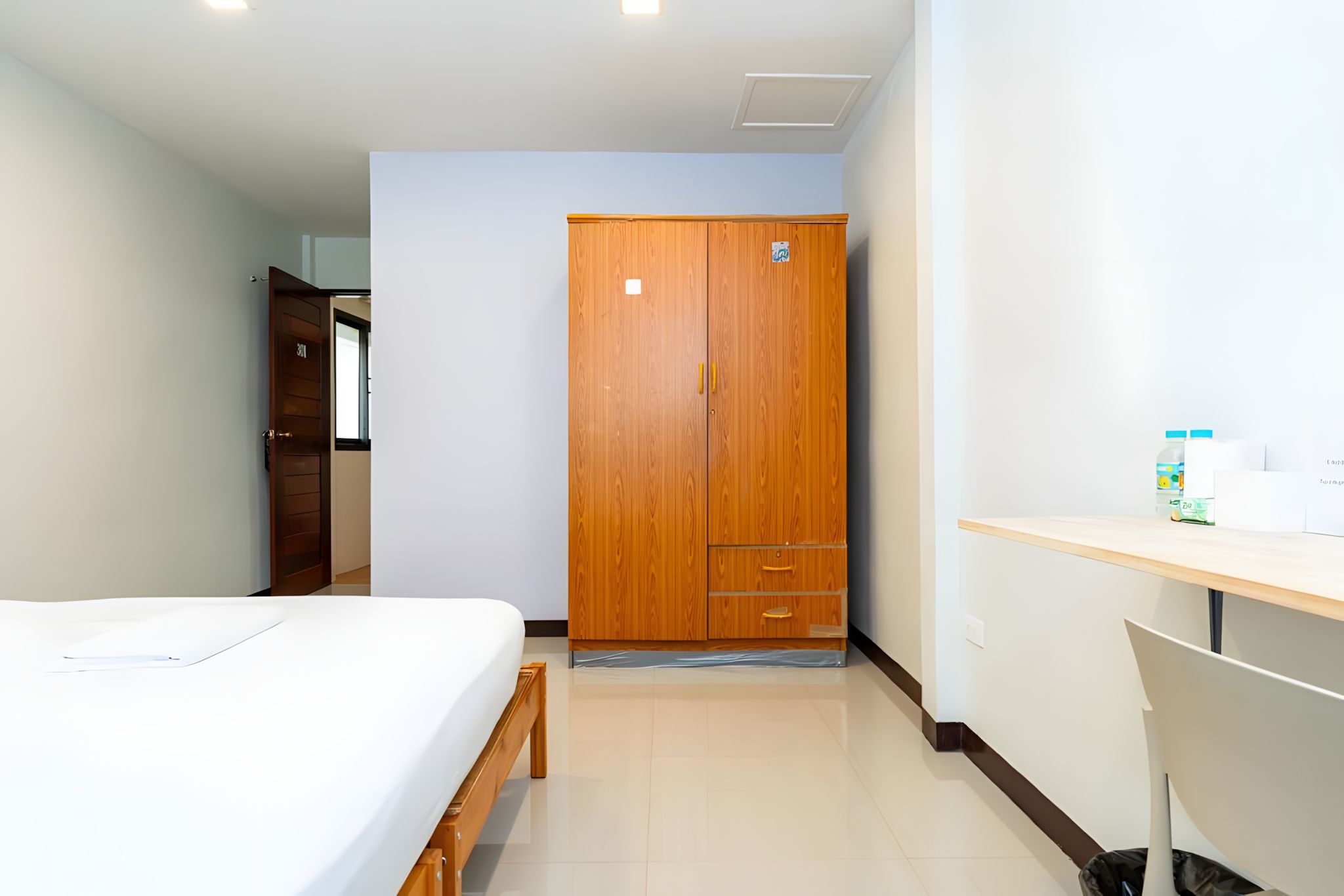 Habitació d'hotel amb un llit, un armari de fusta, un escriptori amb una cadira i una petita estant amb articles de tocador.