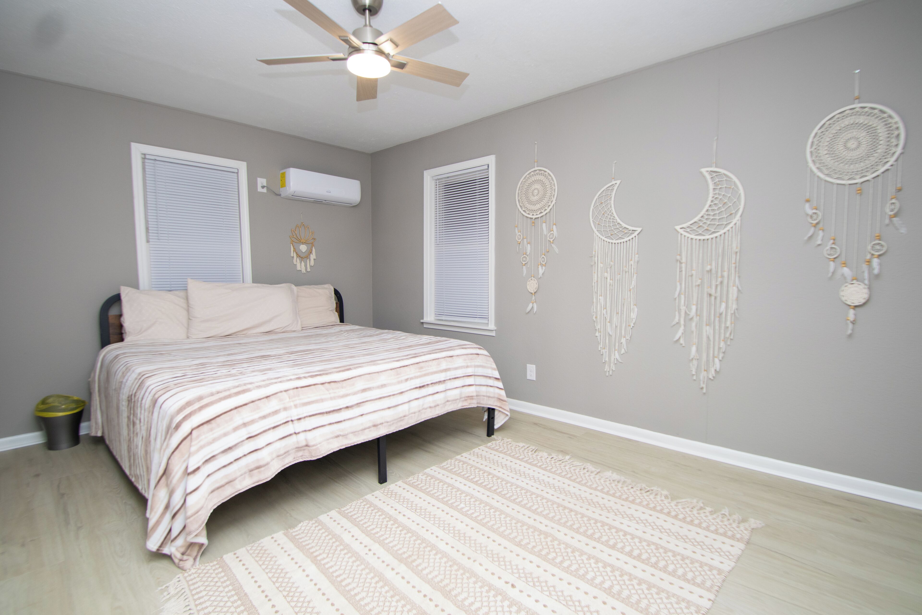 Un dormitorio con cama, ventilador de techo, aire acondicionado instalado en la pared y atrapasueños decorativos.