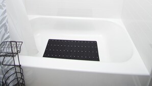 Una bañera blanca con piso de rejilla negra, una ducha y un estante metálico.