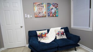 Una habitación con un sofá azul oscuro, dos almohadones decorativos, una puerta blanca y dos obras de arte colgadas en la pared.