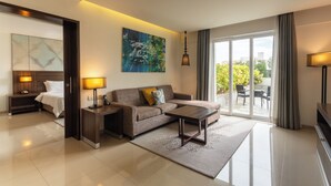 Ein modernes Hotelzimmer mit Sofa, Couchtisch, Schreibtisch, Lampe, einem Gemälde und Blick ins Freie.