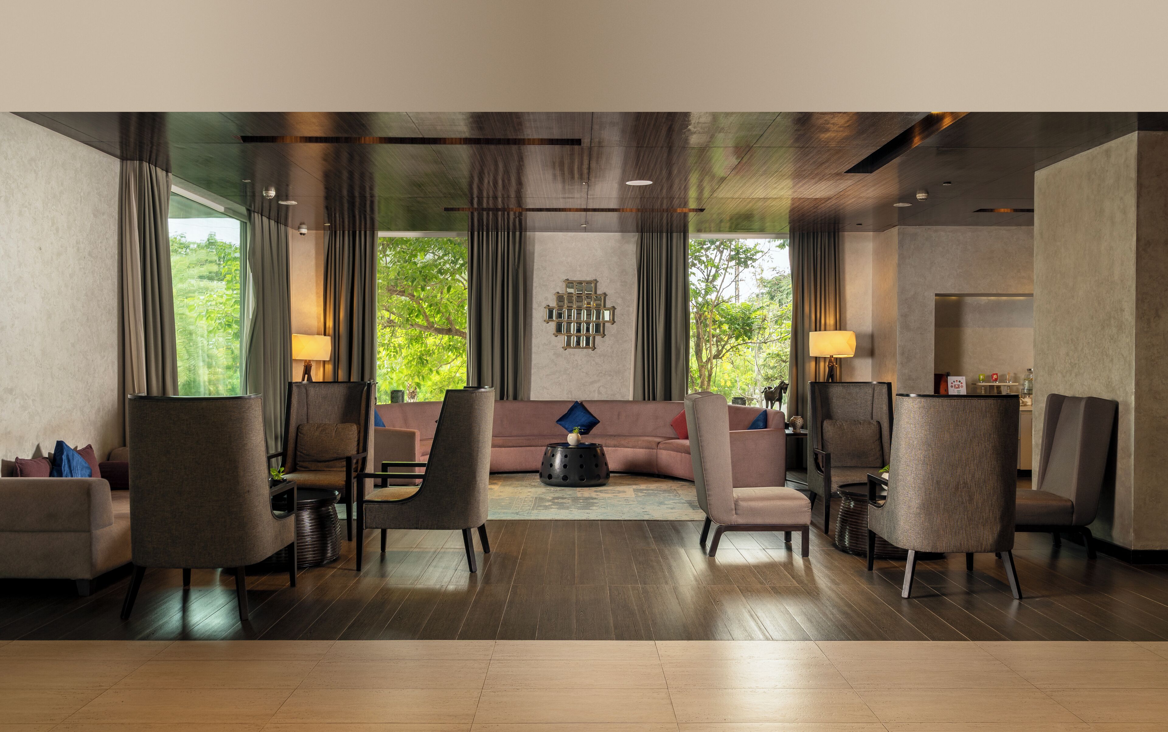 En modern hotellobby med en soffa, stolar, ett soffbord och utsikt över grönområden.
