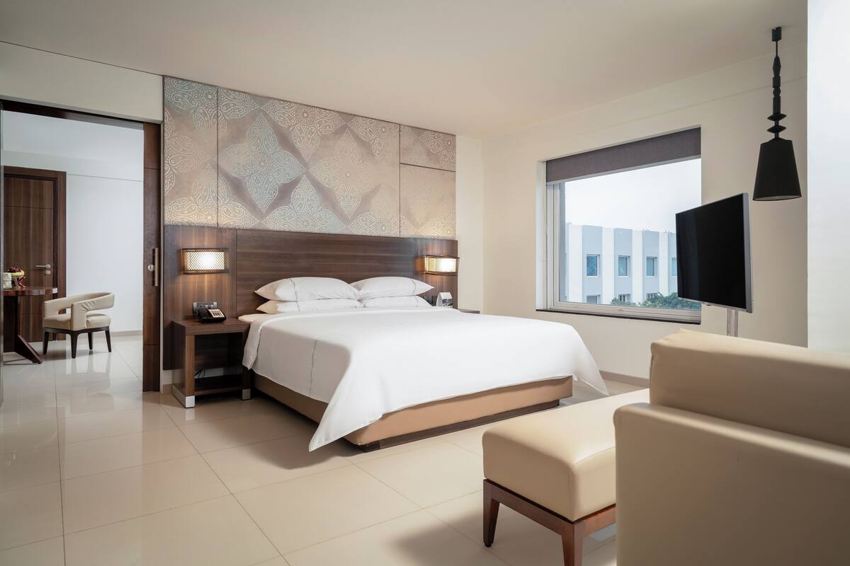 Una habitación de hotel moderna con una cama grande, lámparas de noche, televisión y vistas a edificios.