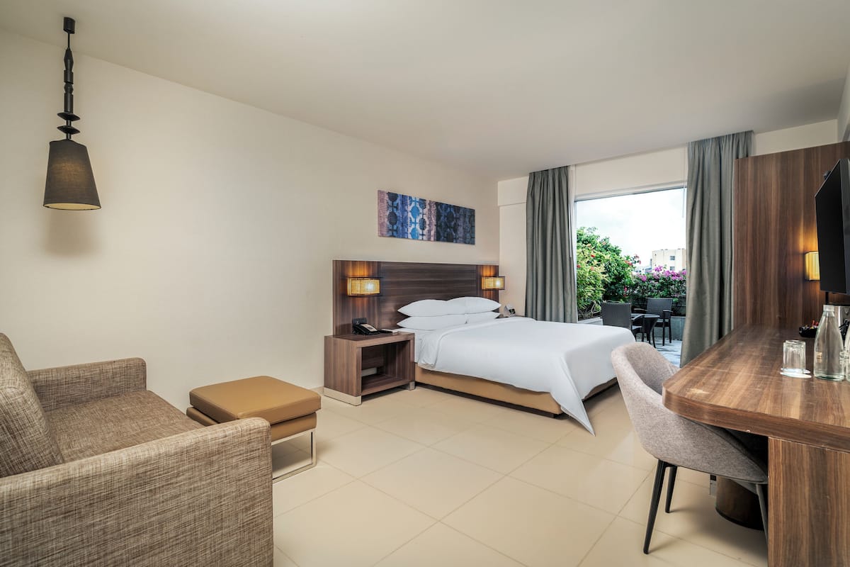 Una habitación de hotel con cama, escritorio, silla, sofá, mesita de noche y lámpara colgante.