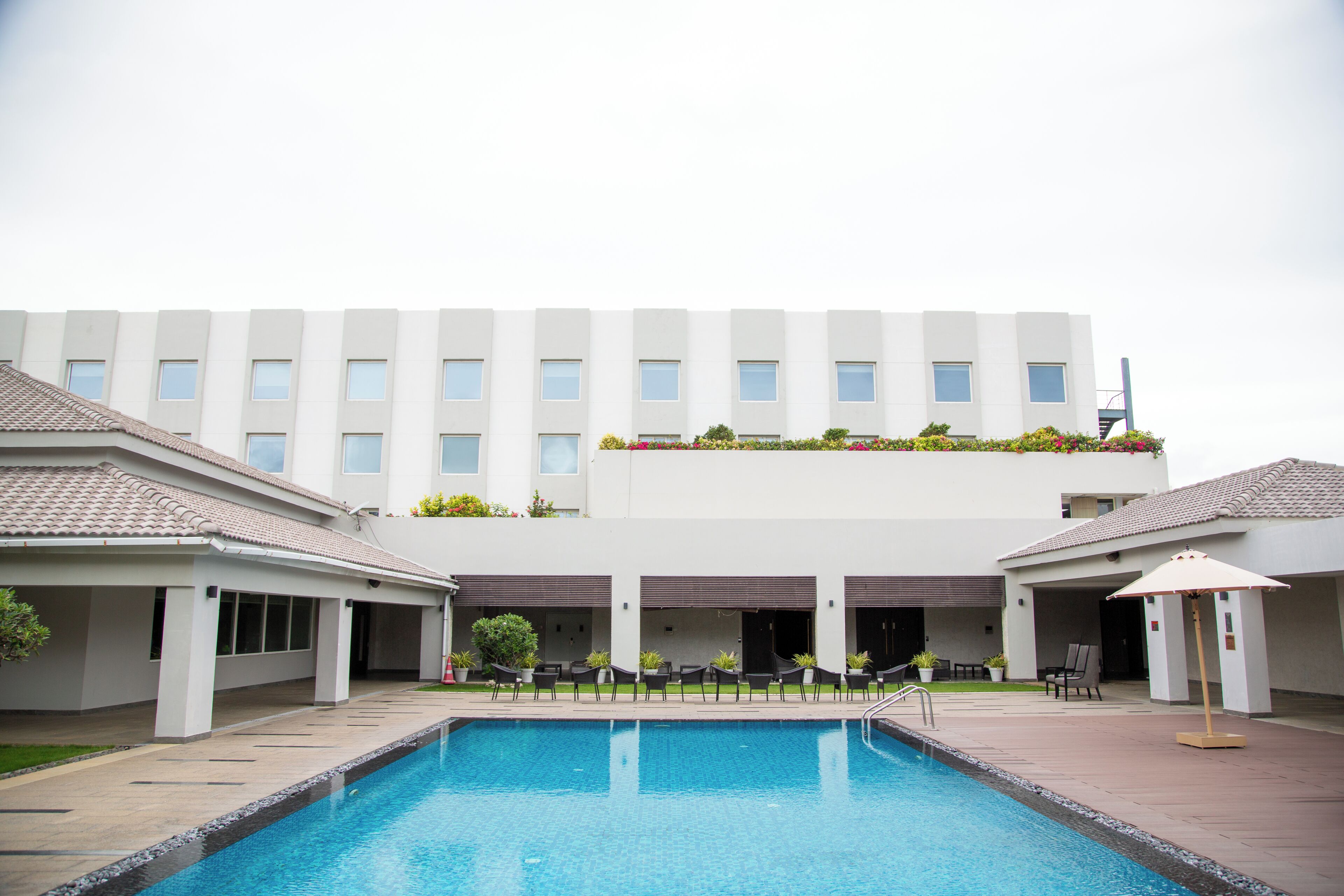 A swimming pool with a tiled deck, a building with multiple windows, and outdoor seating.