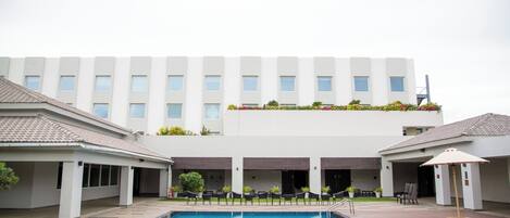 A swimming pool with a tiled deck, a building with multiple windows, and outdoor seating.