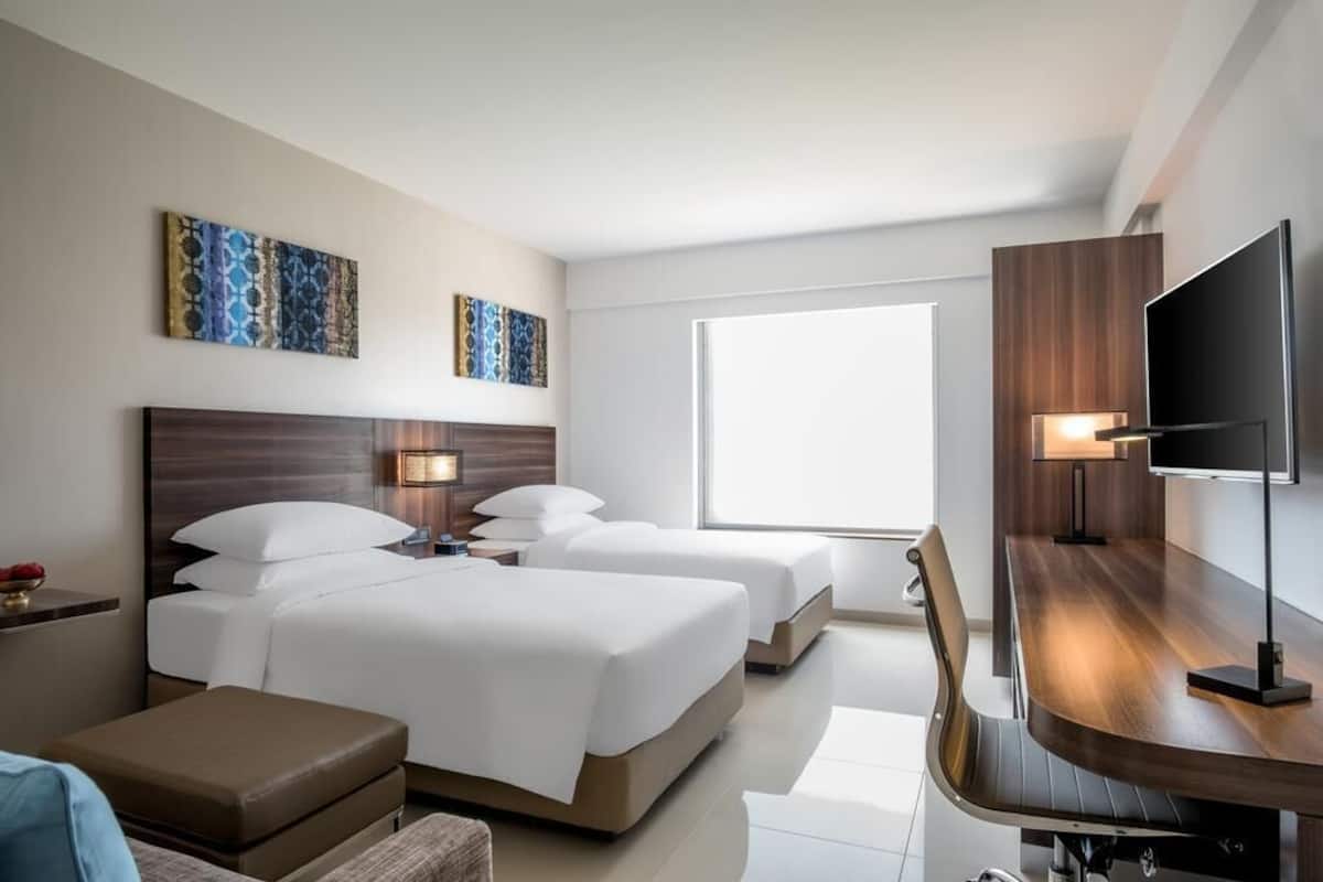 Habitación de hotel con dos camas, un escritorio, un televisor y obras de arte en las paredes.