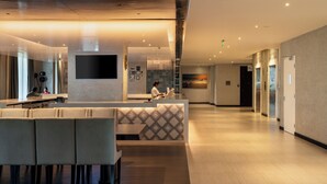 Eine moderne Hotelhalle mit Rezeption, Sitzgelegenheiten und einem großen Fernseher.