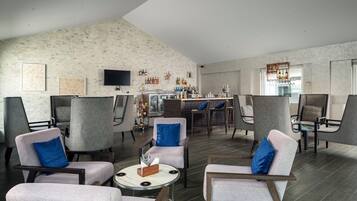 Ein moderner Lounge-Bereich mit verschiedenen Sitzgelegenheiten, einer Bar mit zahlreichen Flaschen und einem an der Wand befestigten Flachbildfernseher.