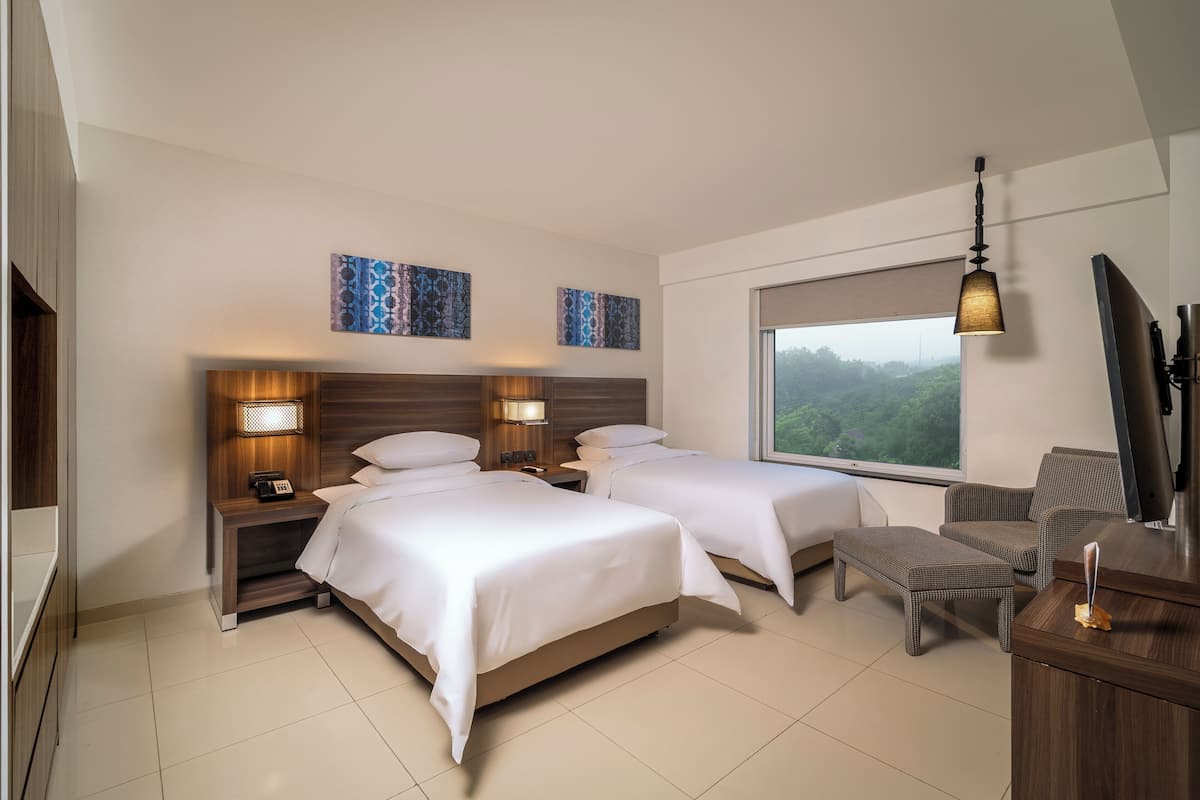 Habitación de hotel con dos camas, un escritorio, una silla, un televisor y una ventana con vistas.