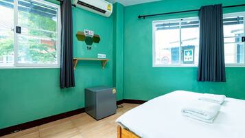 A room with teal walls, a bed with white linens, a small gray cabinet, a window with curtains, and an air conditioning unit.