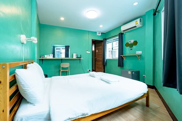 A hotel room with a bed, a desk, a chair, an air conditioning unit, and a window with curtains. - GO INN The Giant Swing (Bangkok)