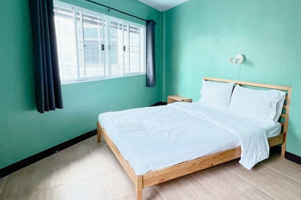 Une pièce avec un lit, une fenêtre avec des rideaux et un luminaire au plafond.