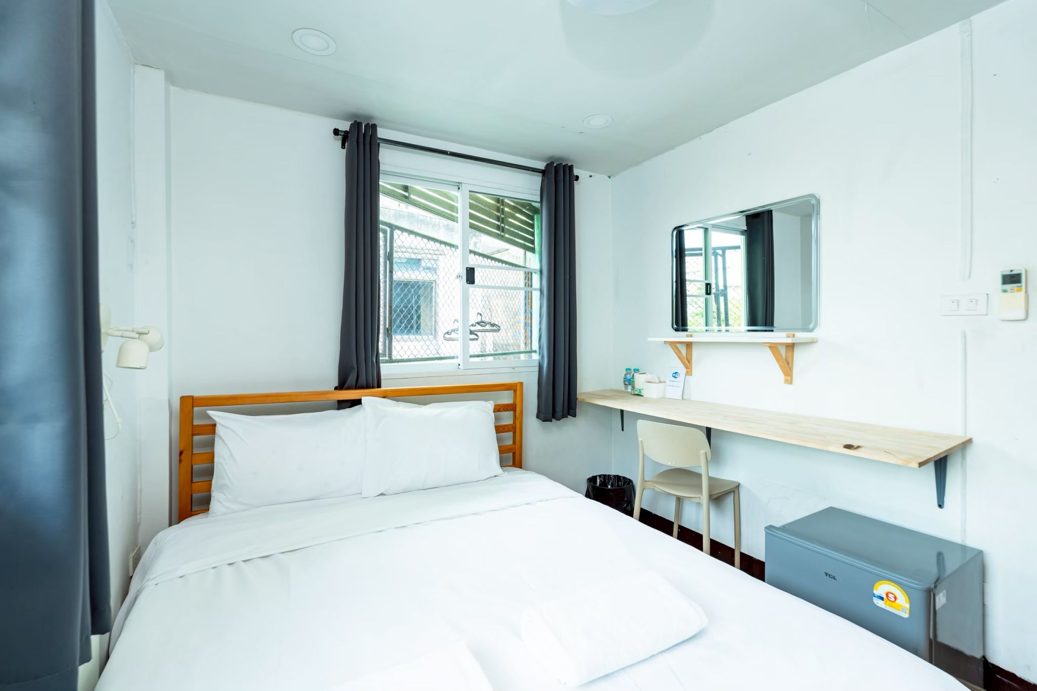 A hotel room with a bed, a desk with a chair, a mirror, and a small cabinet.
