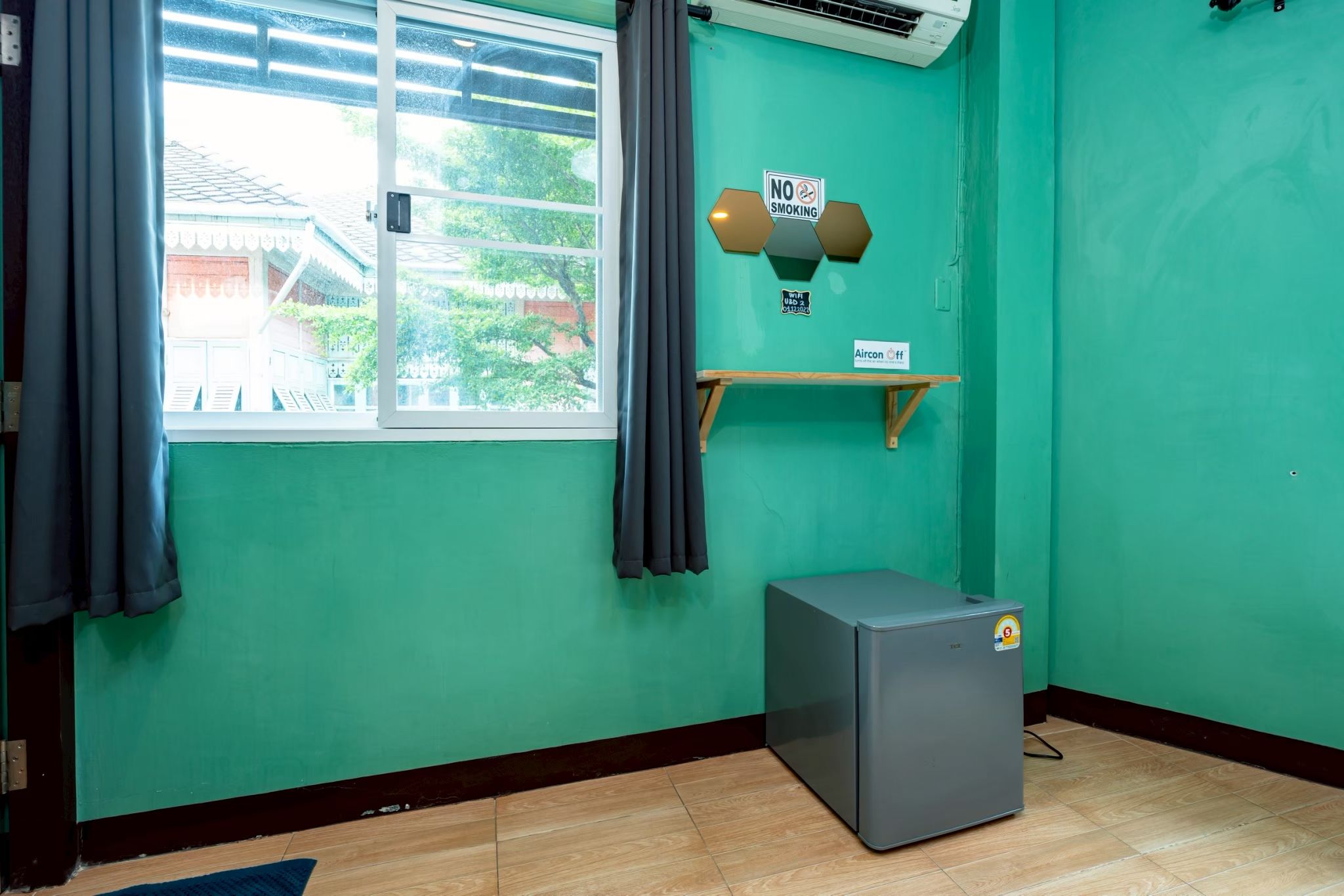 Ein Zimmer mit Fenster, einer Wand-Klimaanlage, einem kleinen Kühlschrank und einem 'RAUCHVERBOT'-Schild.