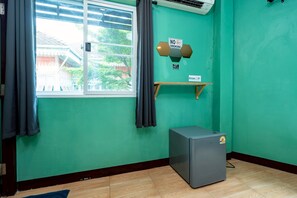 Een kamer met een raam, een wandairconditioner, een kleine koelkast en een 'ROOKVRIJ' bord.
