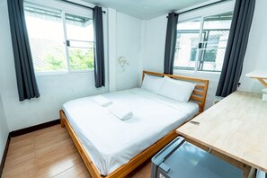 Habitación individual con una cama y cabecera de madera, una mesita de noche pequeña y una ventana con cortinas.