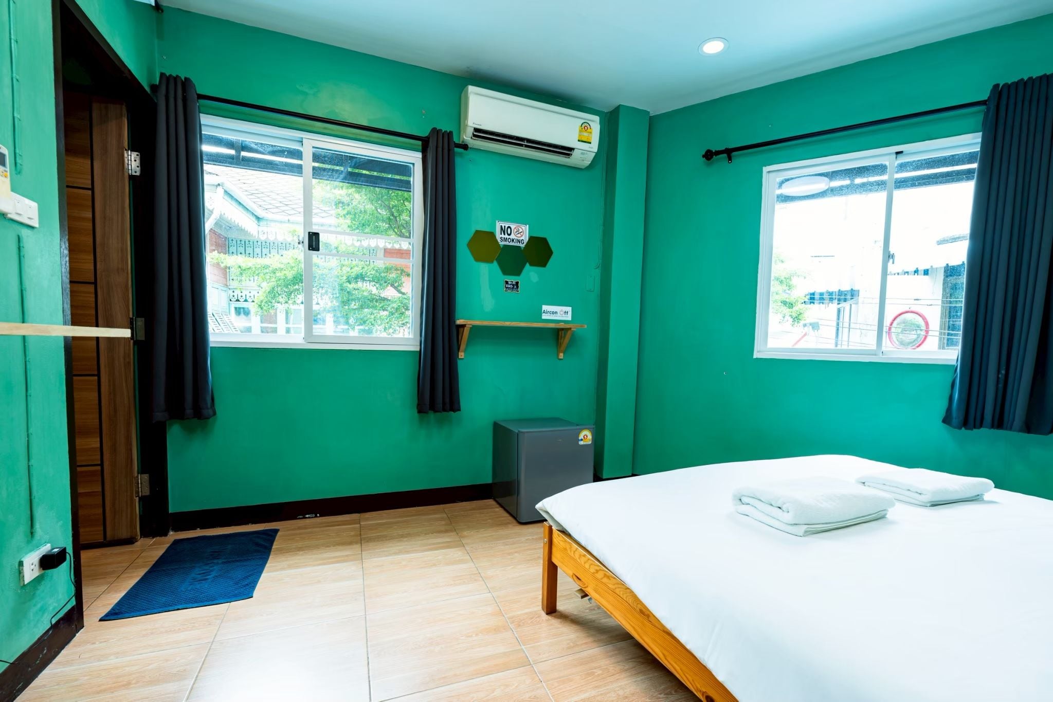 A room with a bed, a window, an air conditioning unit, a small heater, and a door.