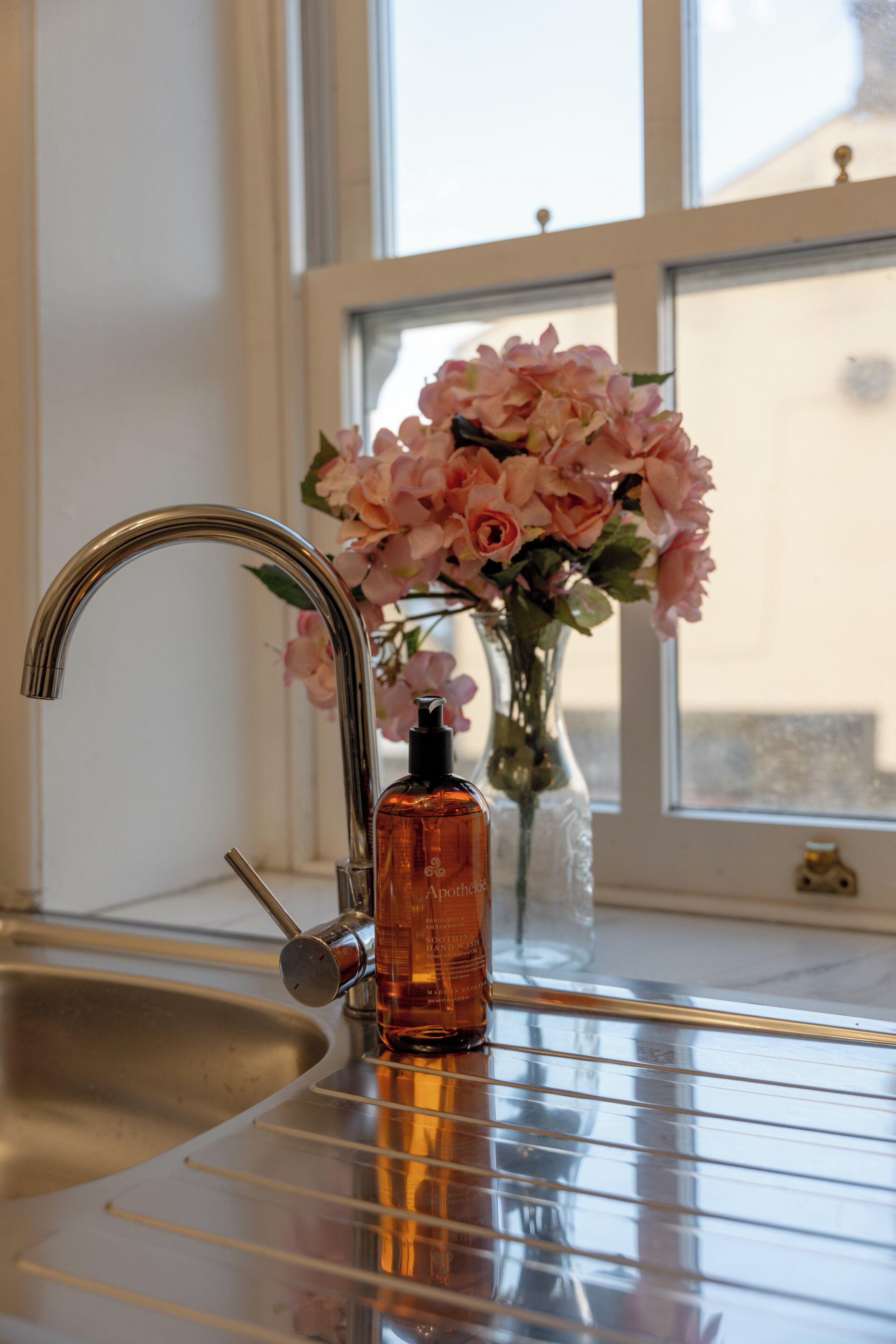 A bathroom sink with a modern faucet, a glass vase with pink flowers, and a bottle of soap.