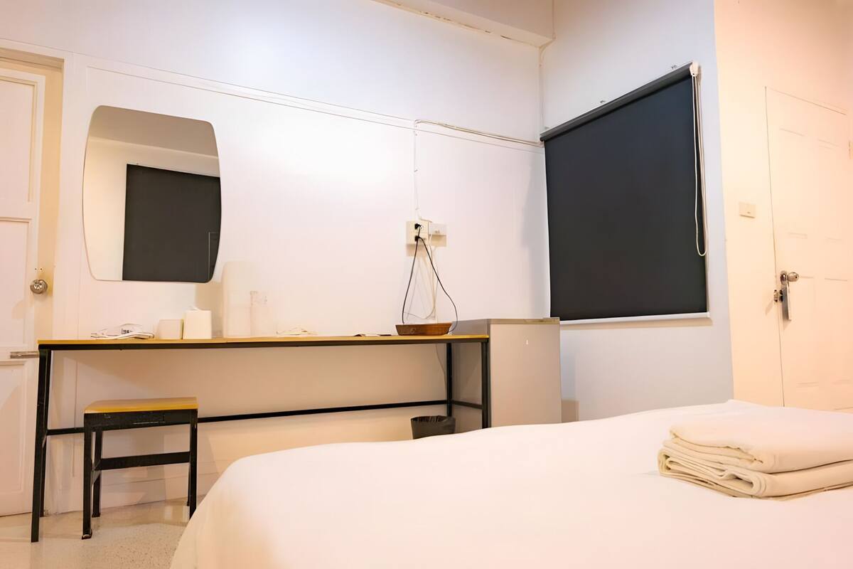 Een hotelkamer met een bed, een bureau met stoel, een spiegel en een raam.