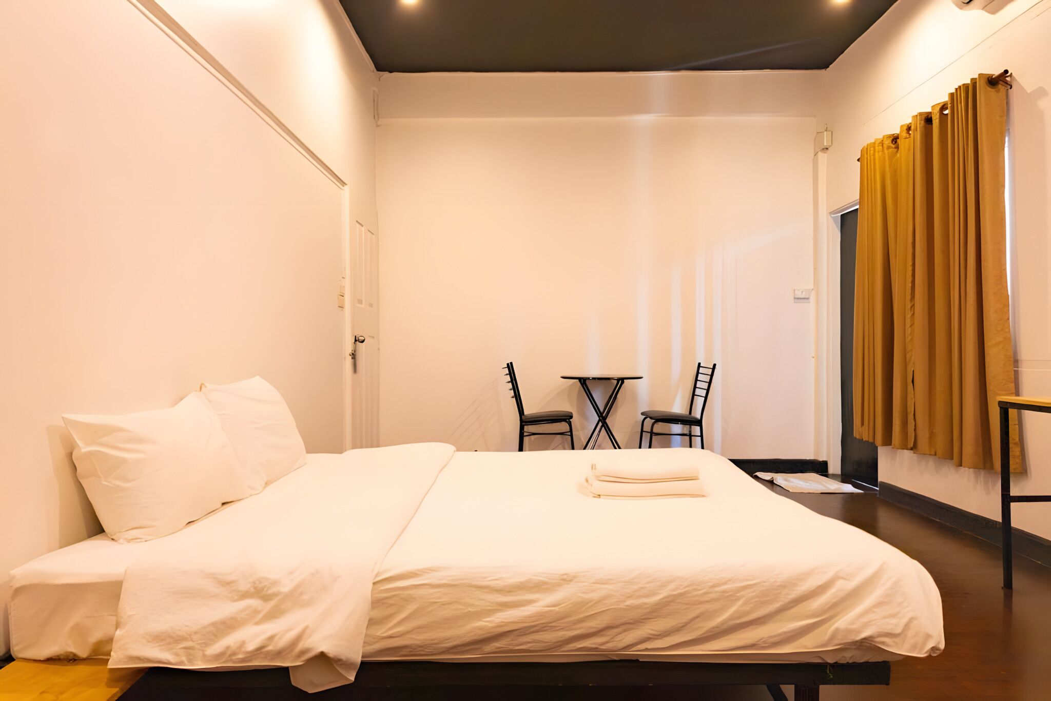Una habitación de hotel con una cama, una mesita con sillas y una ventana con cortinas.