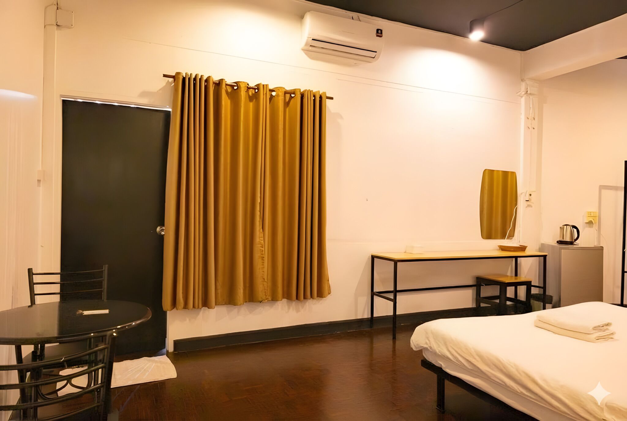 A hotel room with a bed, a desk, a chair, a table, a curtain, and an air conditioning unit.