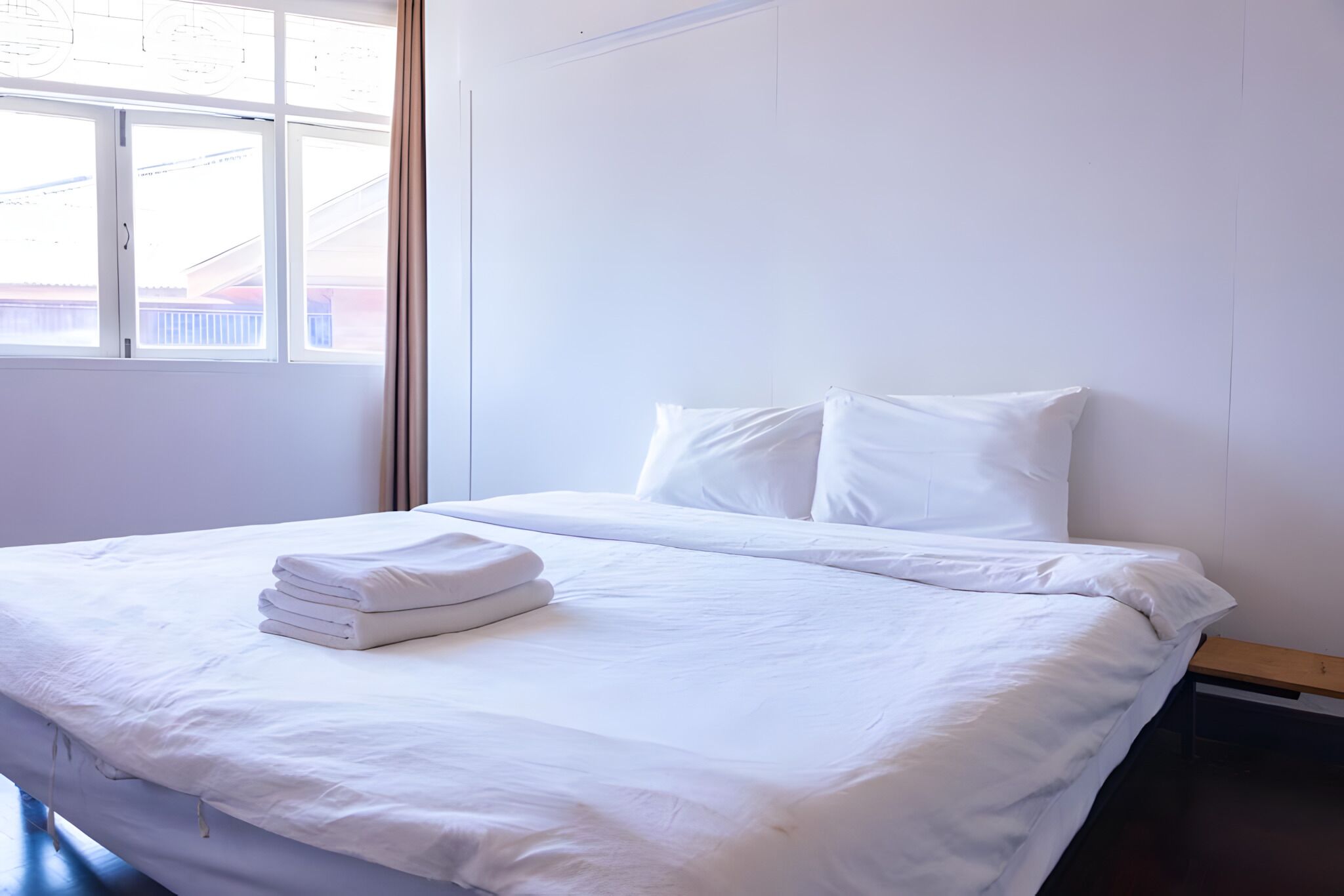 A clean, white hotel room with a bed, a window, and a wooden nightstand.