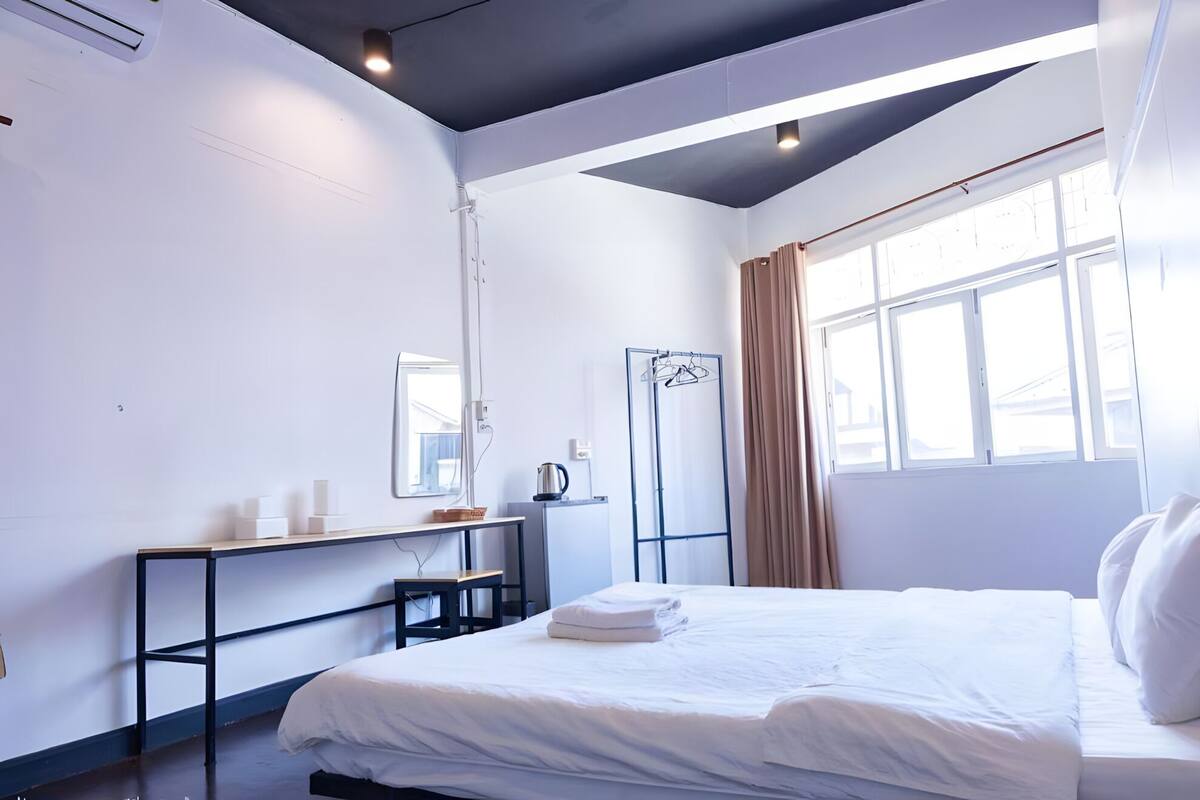Een hotelkamer met een bed, een bureau, een spiegel, een raam met gordijnen en een radiator.