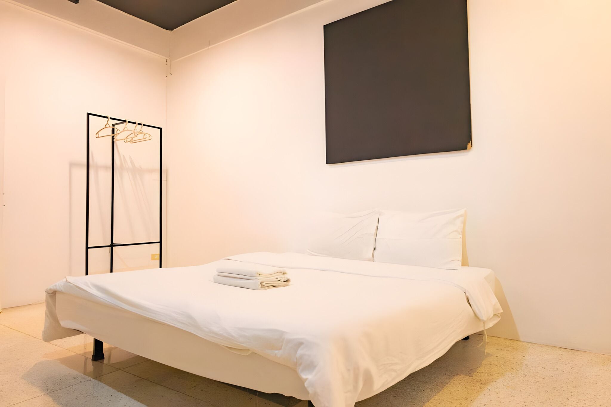 A modern bedroom with a bed, white linens, a black-framed mirror, and a plain wall.