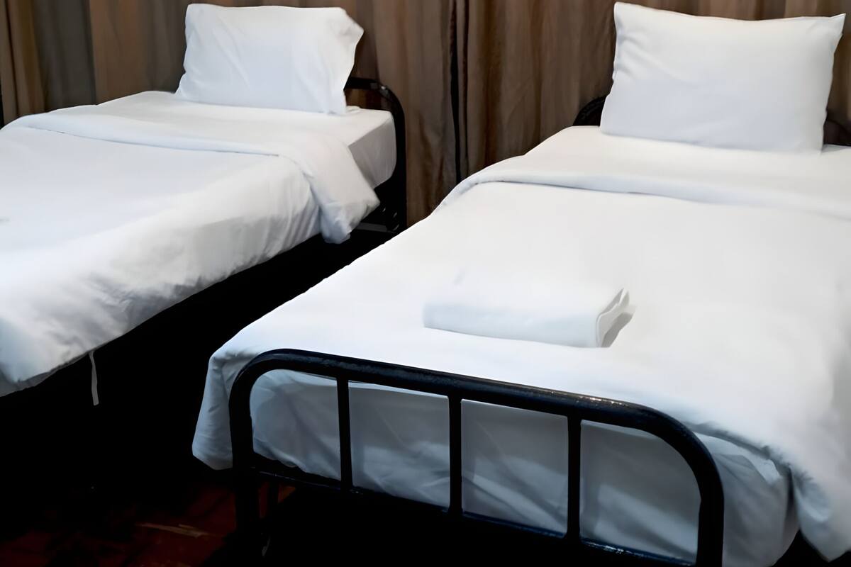 Een hotelkamer met twee enkele bedden, een houten vloer en een gordijnen achtergrond.