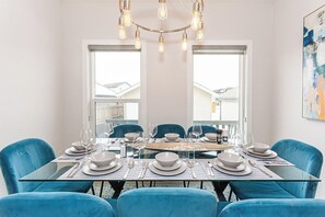 A dining area with a glass table, blue chairs, and a chandelier. - Where Luxury Feels Like Home | Cozy, Comfy and Spacious 4-Bedroom Retreat (Edmonton)