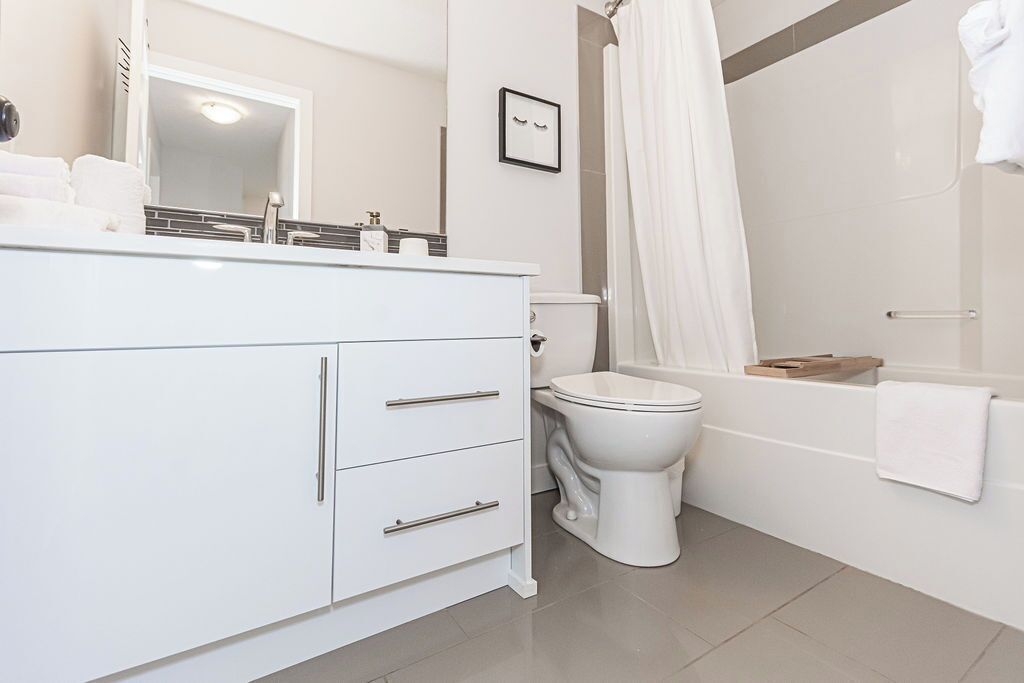 A modern bathroom with a white vanity, a toilet, a bathtub, and a shower curtain.