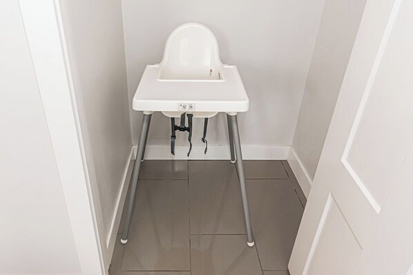 A white high chair in a corner of a room with a tiled floor and white walls. - Where Luxury Feels Like Home | Cozy, Comfy and Spacious 4-Bedroom Retreat (Edmonton)