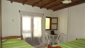 A room with two beds, a desk with a laptop, a chair, a window with curtains, and a wooden ceiling. - La Casa de Jessy (Máncora)
