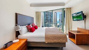 Habitación de hotel con cama, televisión, escritorio y vistas a edificios altos.