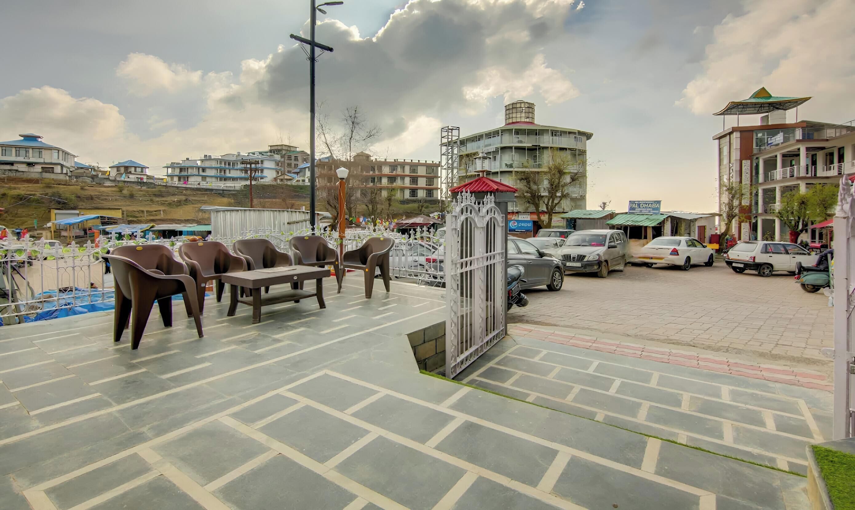 A paved outdoor area with seating, a gated entrance, and parked cars.